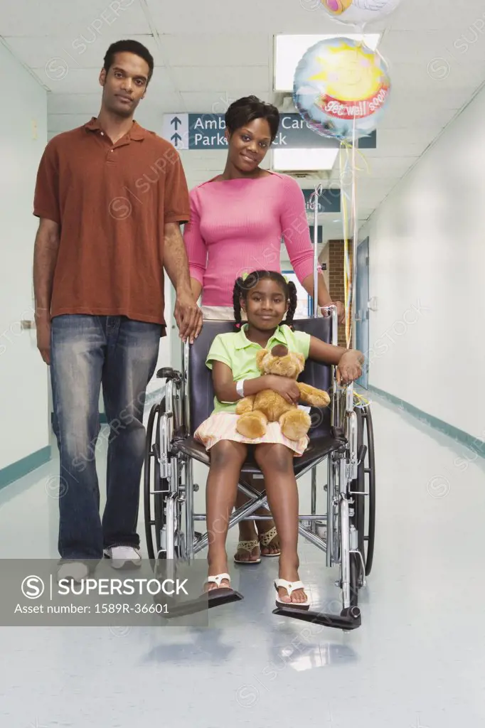 African girl smiling in wheelchair with parents in hospital