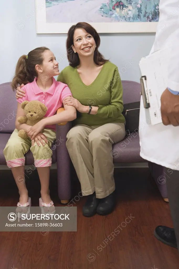 Hispanic mother and daughter talking to doctor in waiting room