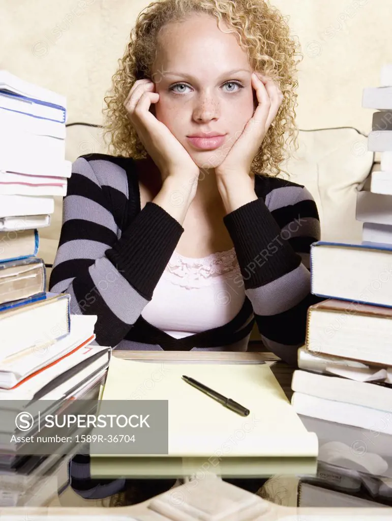 Young woman studying at desk with large stacks of books and notepad
