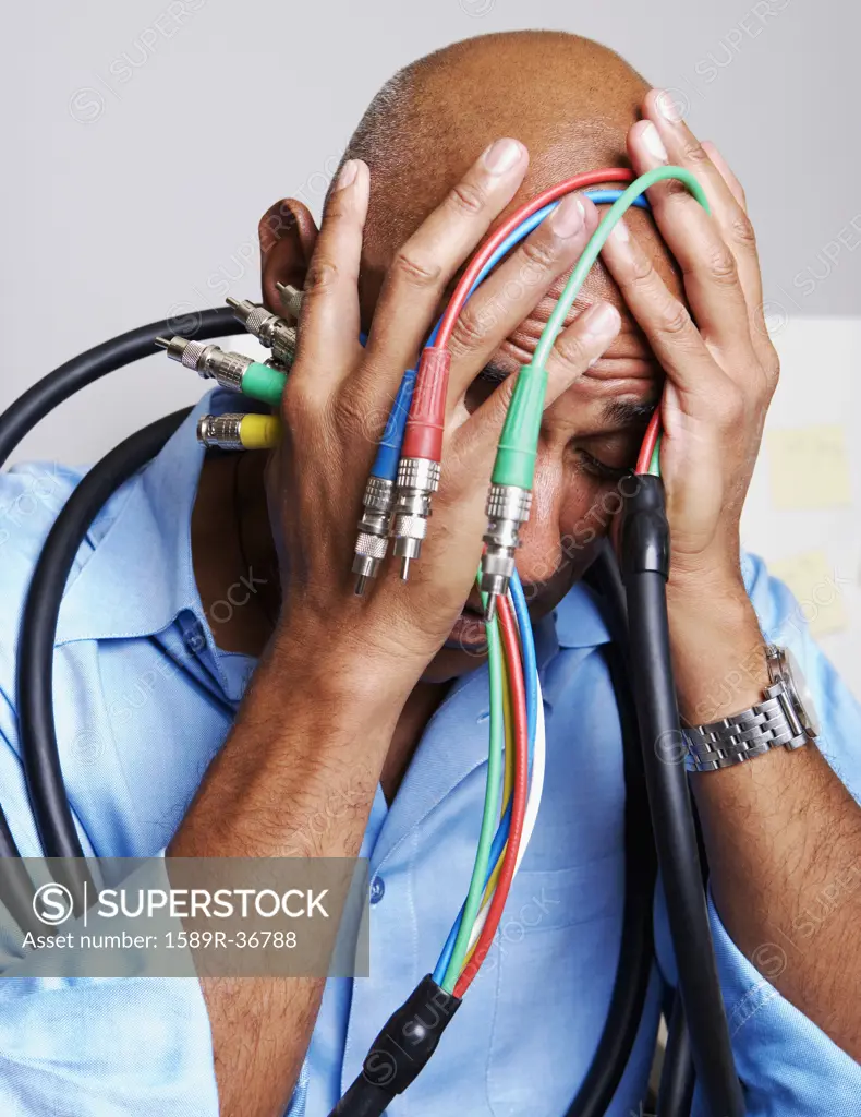 African businessman holding computer cables with head in hands
