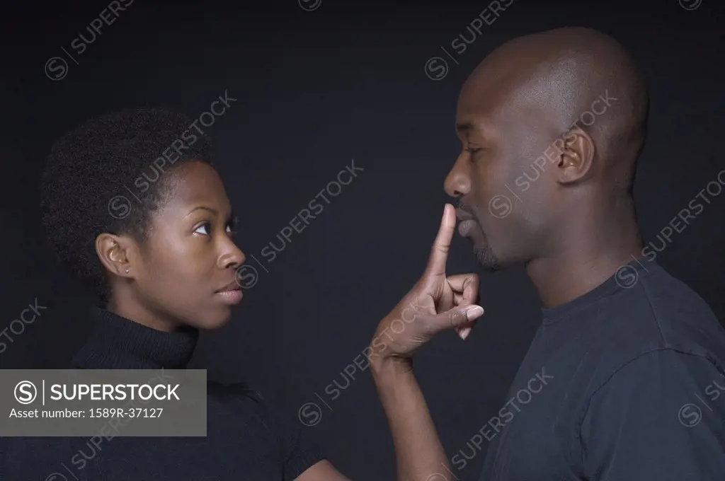 African woman putting finger on boyfriends lips
