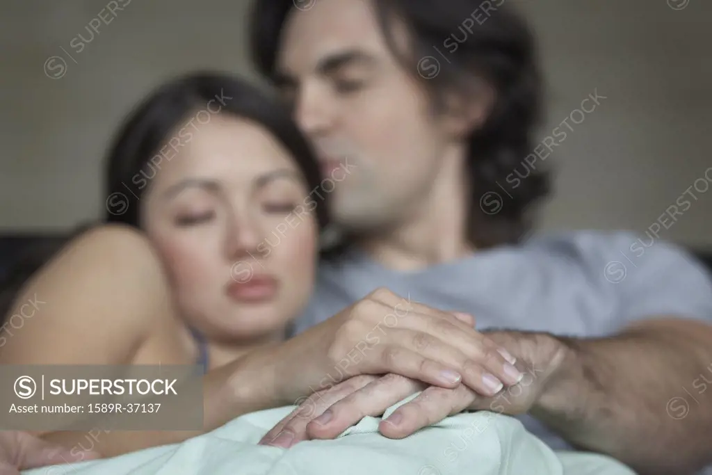 Multi-ethnic couple hugging in bed
