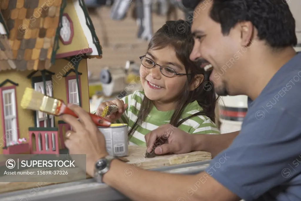 Hispanic father and daughter painting doll house