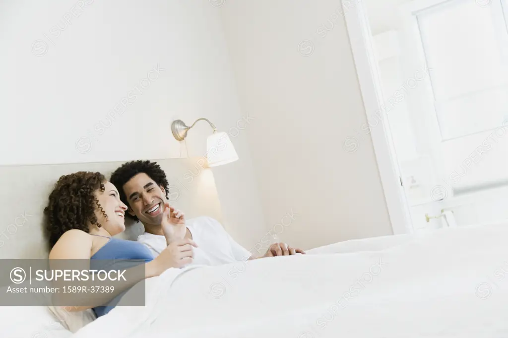 Pregnant African couple laughing in bed