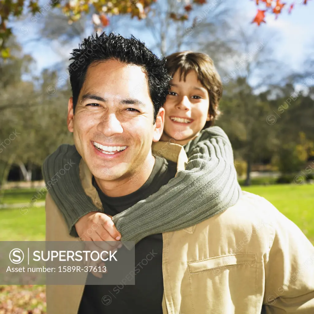 Mixed Race father giving son piggyback ride in park