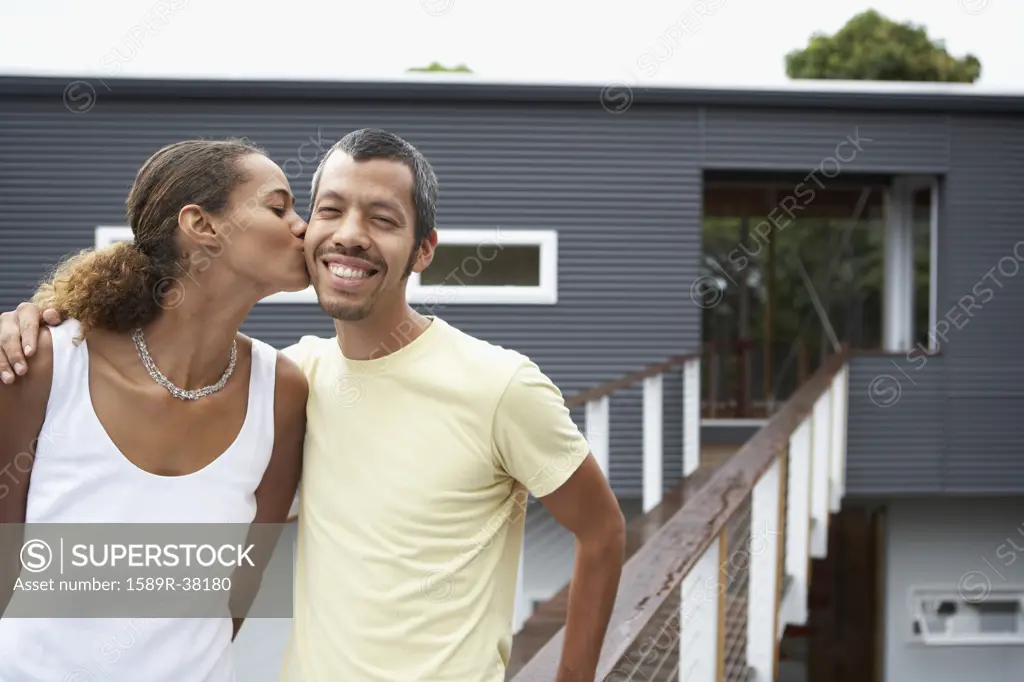 Ethnic-ethnic couple kissing in front of house