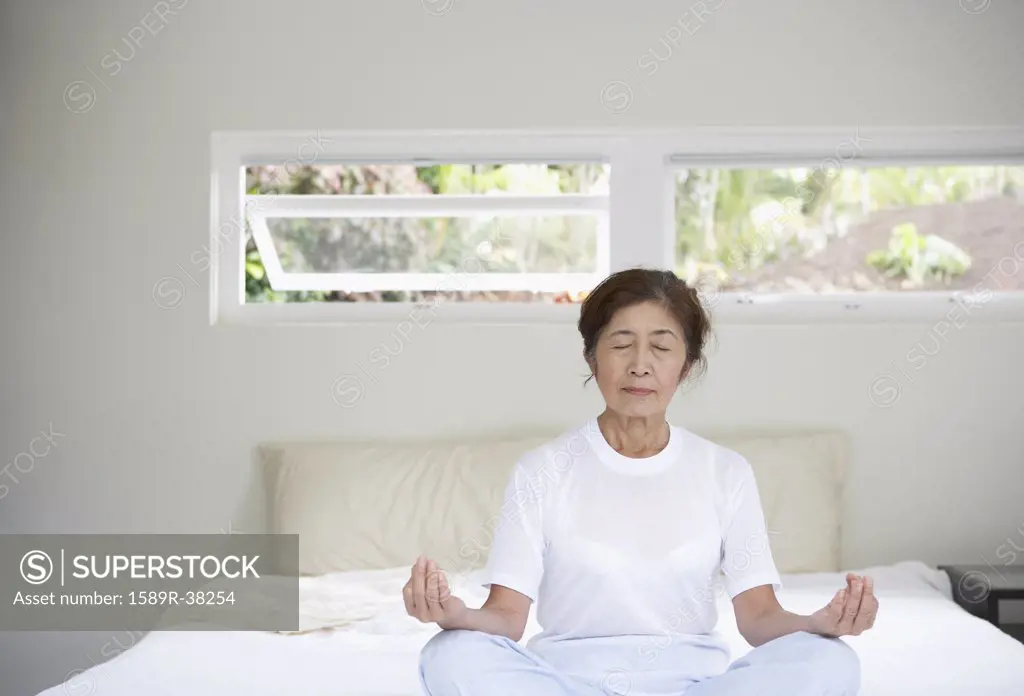 Senior Asian woman meditating on bed