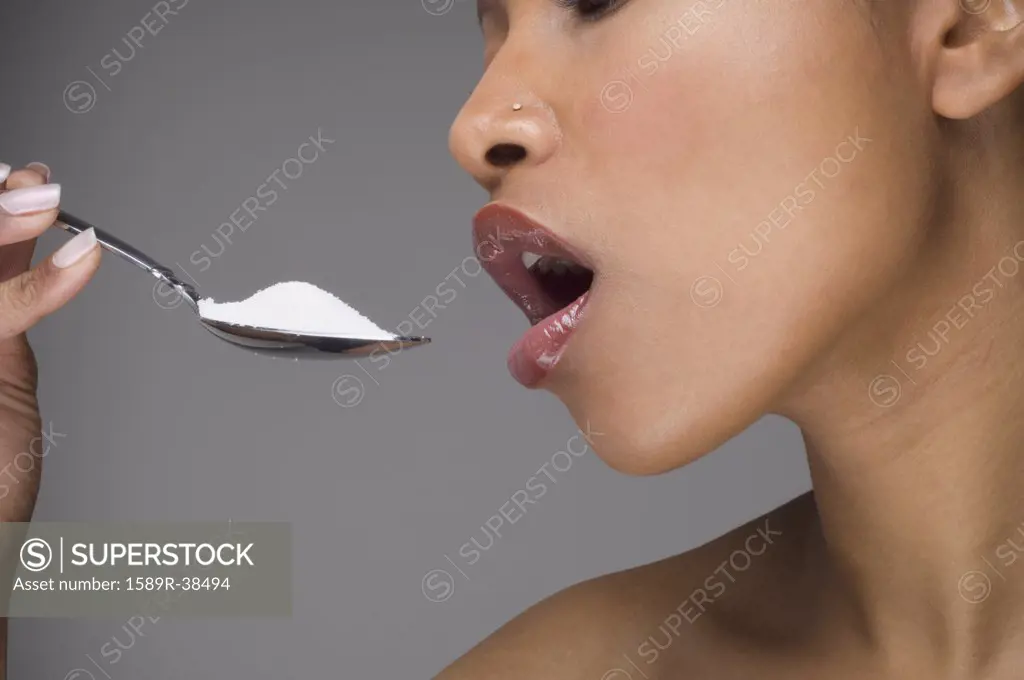 African woman eating spoon of sugar