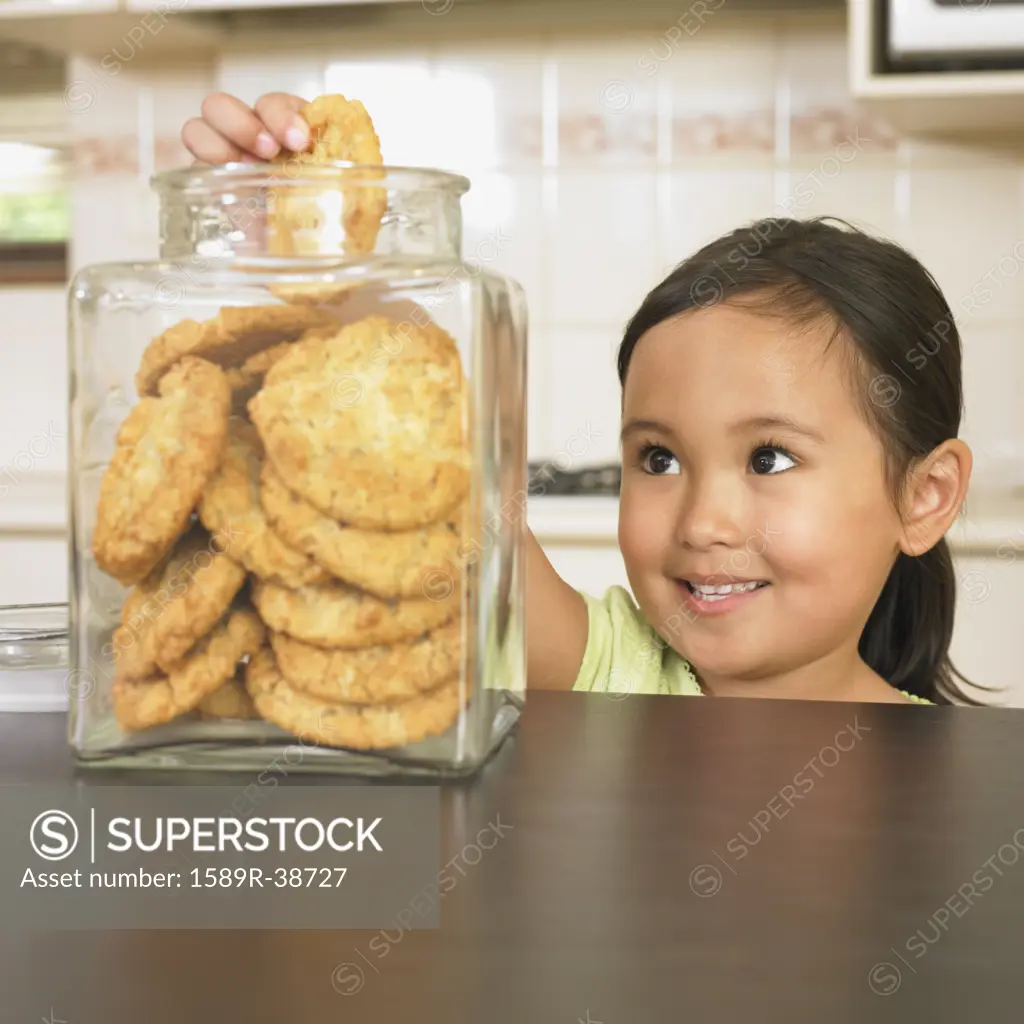 Asian girl taking cookie from jar