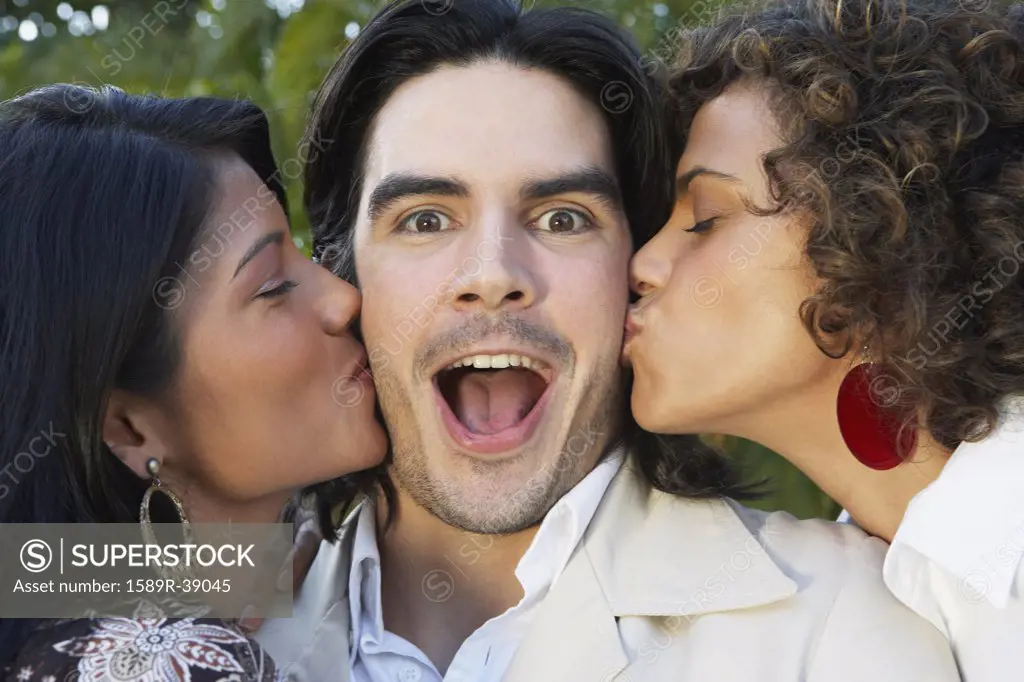 Two women kissing man on cheek