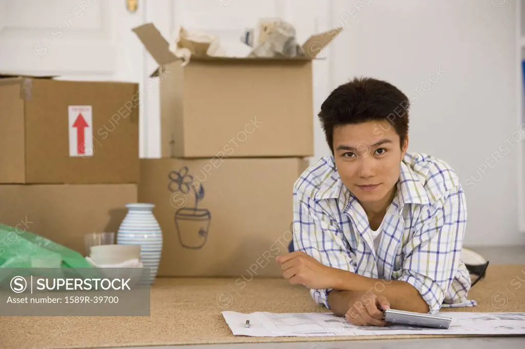 Asian man next to unpacked moving boxes