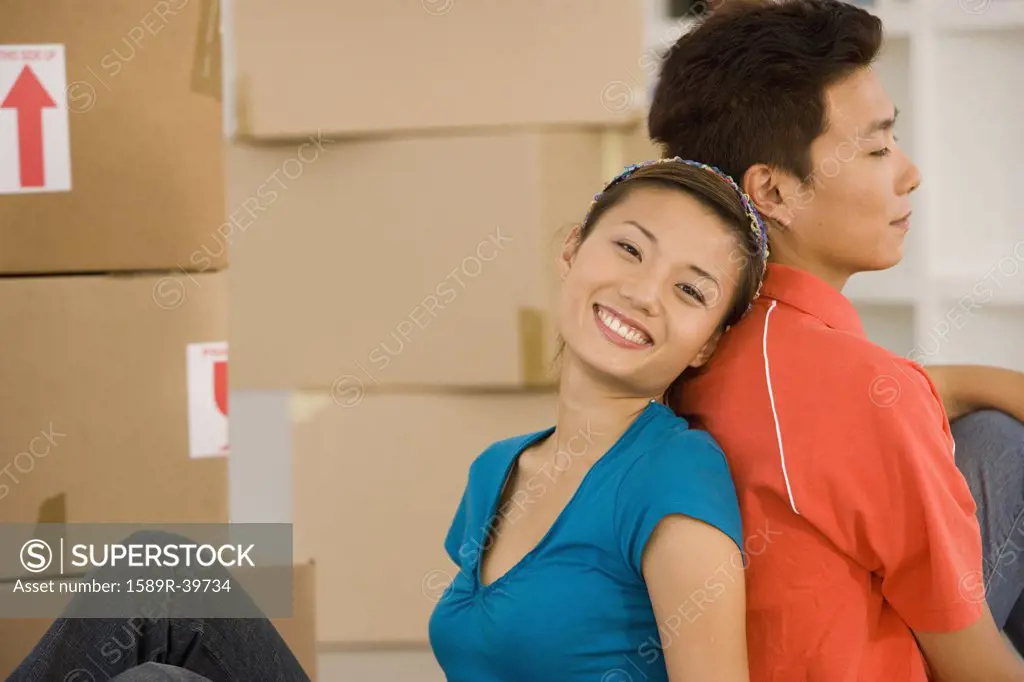 Asian couple sitting back to back next to moving boxes