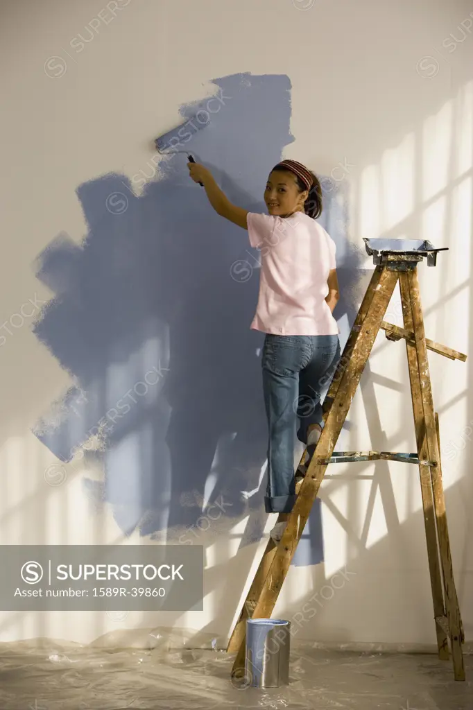 Asian woman painting interior of house