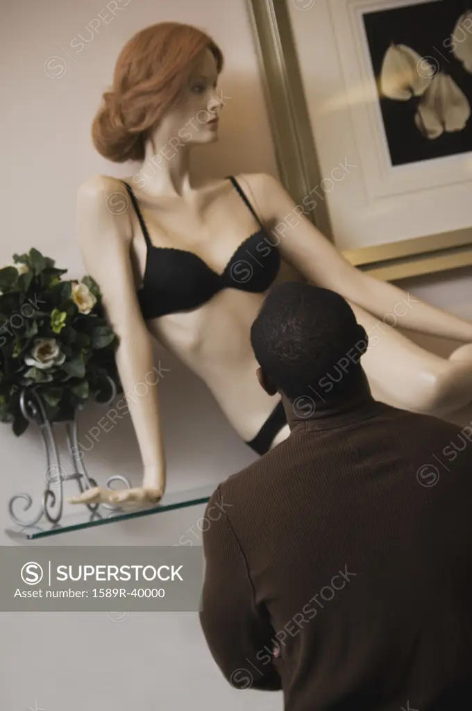 African man looking at lingerie mannequin