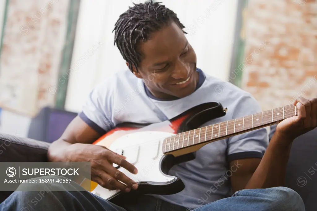 African man playing guitar on sofa