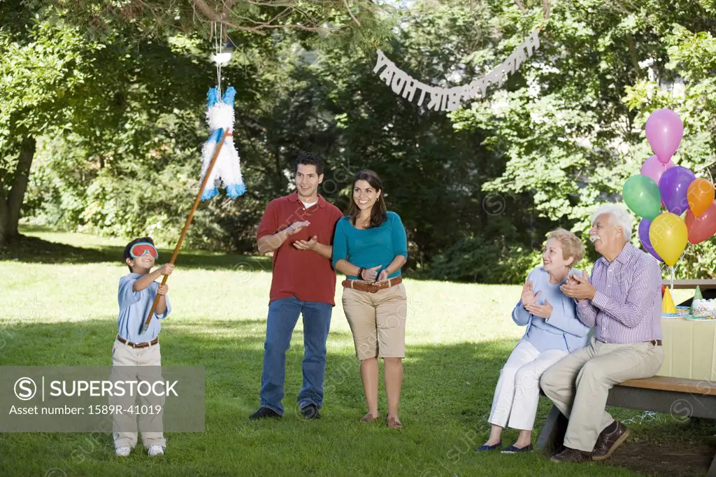 Family watching Hispanic boy hitting pinata at birthday party