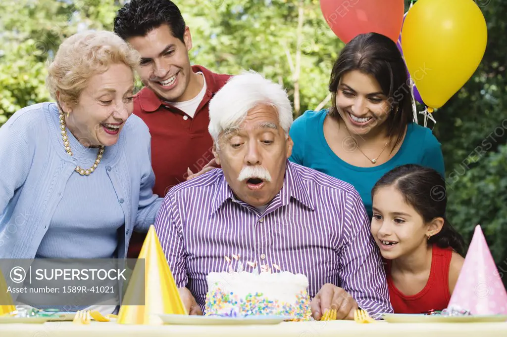 Senior Hispanic man blowing out birthday candles with family in park