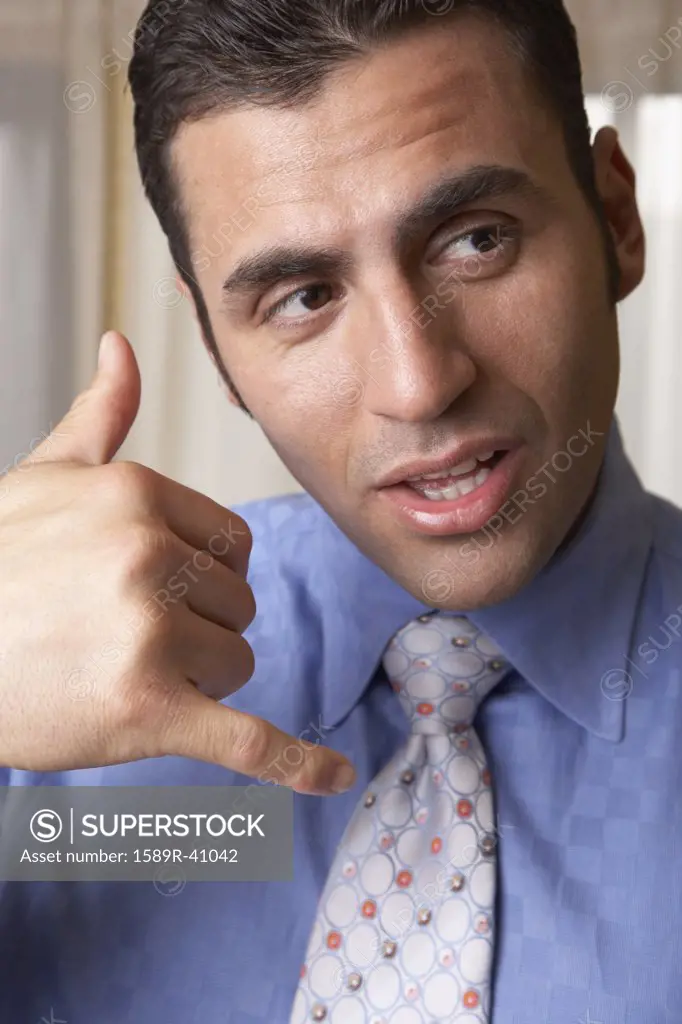 Hispanic businessman mimicking telephone with hand