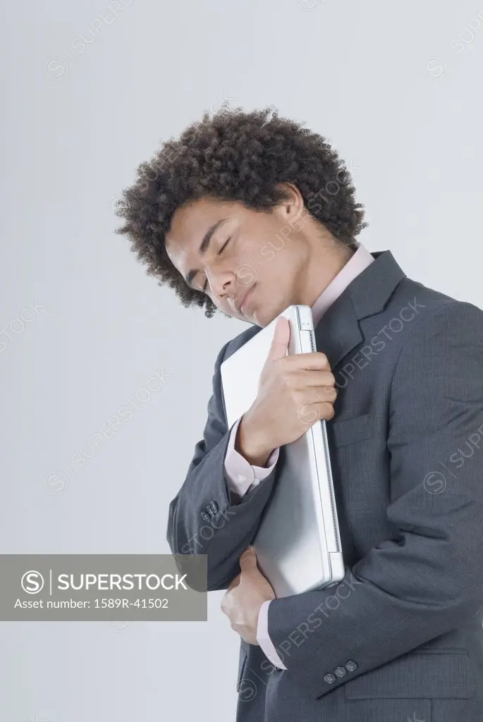Mixed Race businessman hugging laptop
