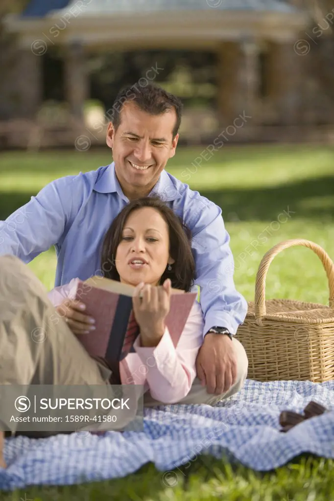 Hispanic couple reading on picnic blanket