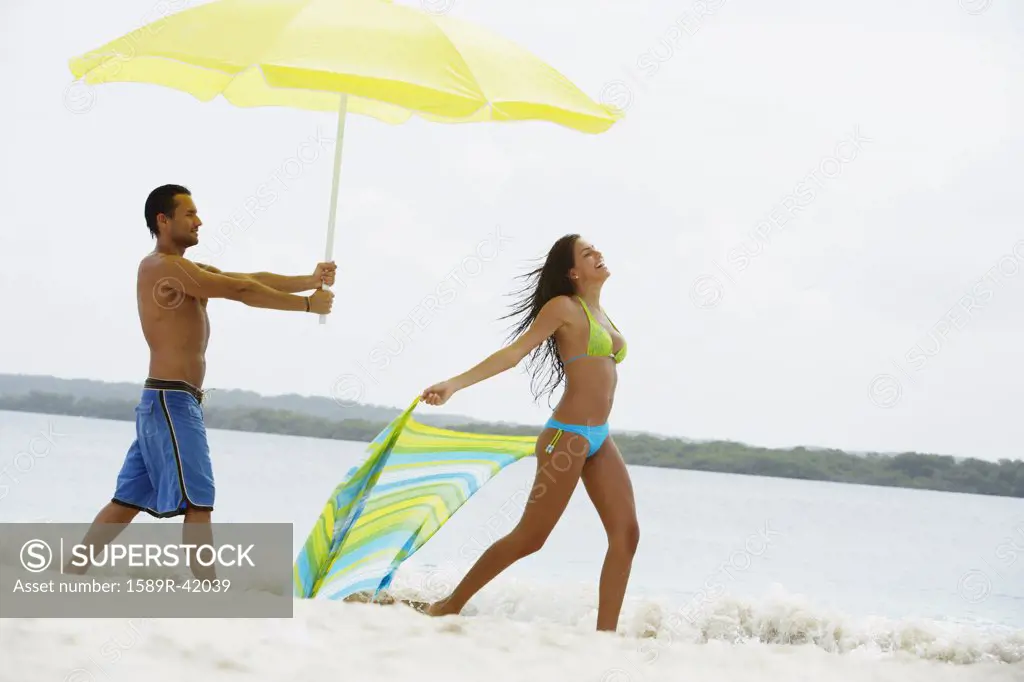 South American man holding umbrella for woman at beach