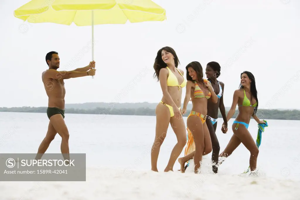 South American man holding umbrella for women at beach