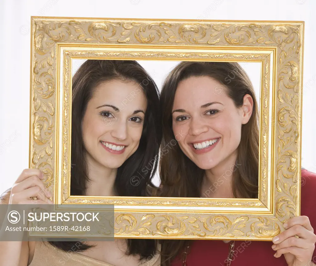 Two young women holding picture frame around faces