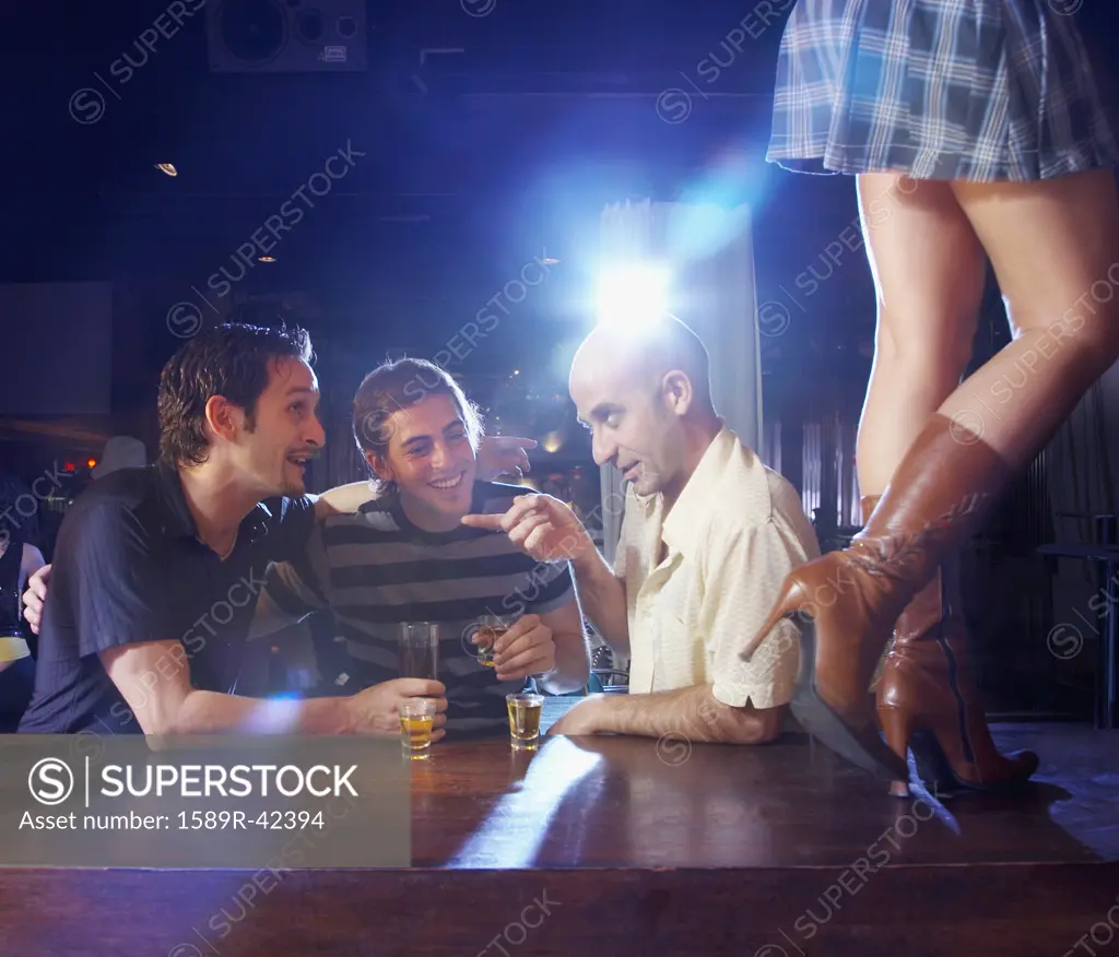Hispanic men watching woman dance on bar