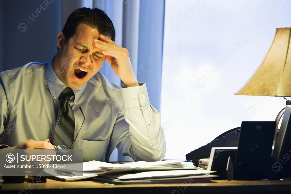 Hispanic businessman yawning at desk