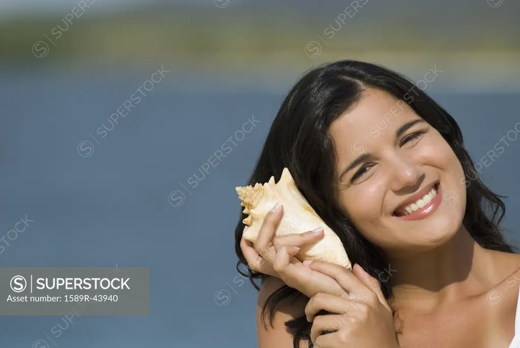 Hispanic woman listening to seashell