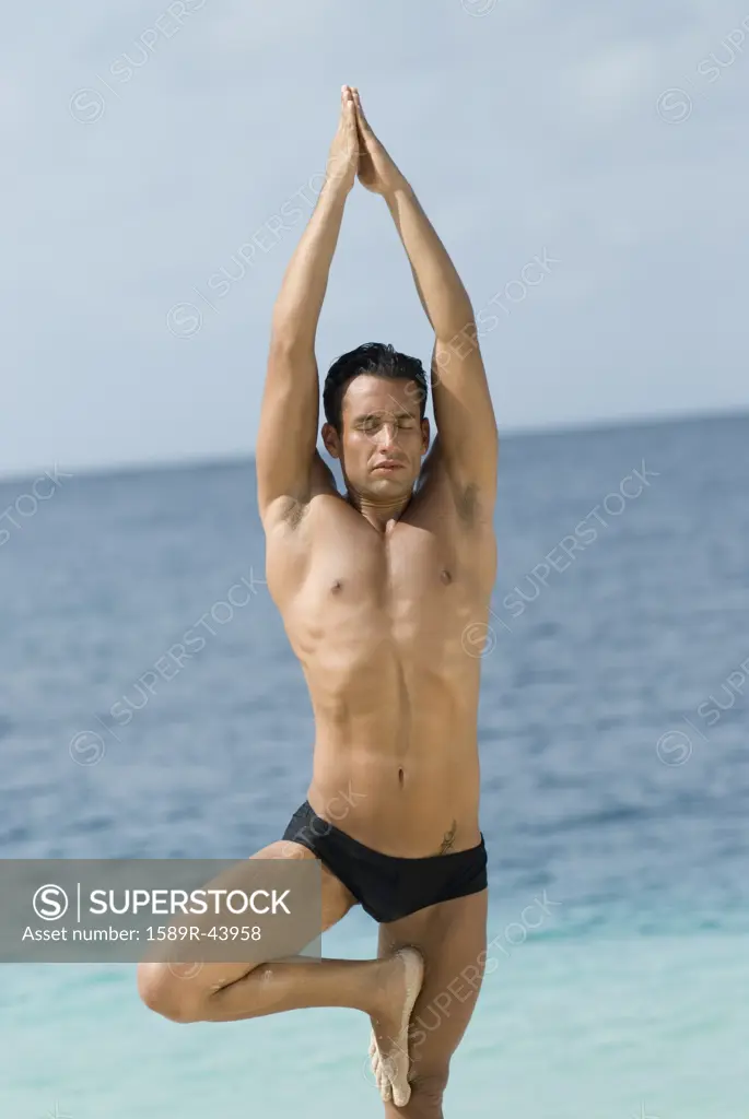 Hispanic man practicing yoga at beach