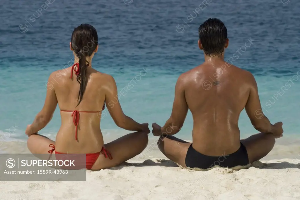 Multi-ethnic couple meditating at beach