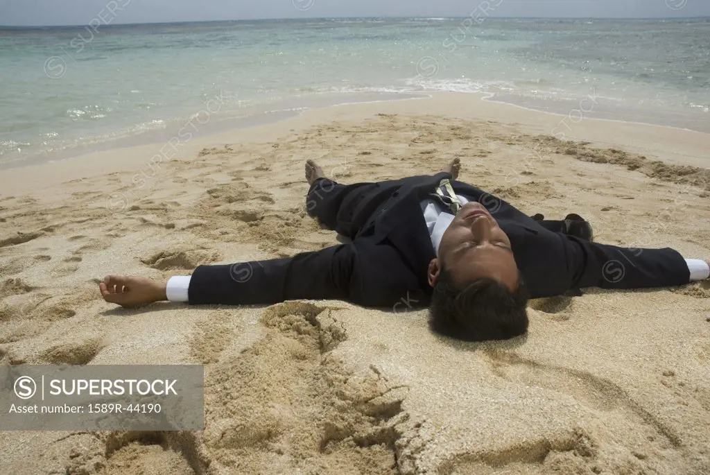 Hispanic businessman laying on beach