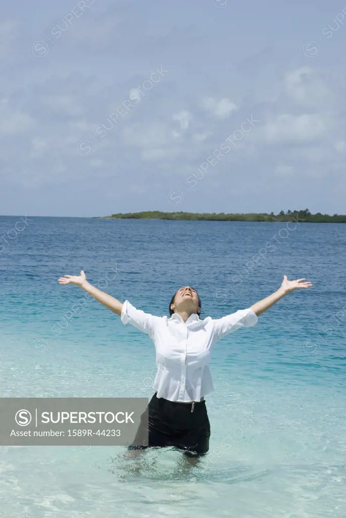 Hispanic businesswoman in water with arms raised