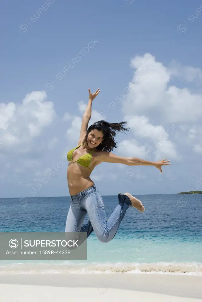 Hispanic woman jumping at beach