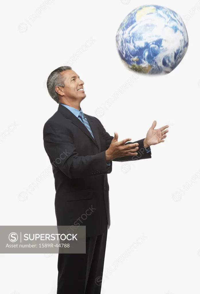 Hispanic businessman throwing globe in air
