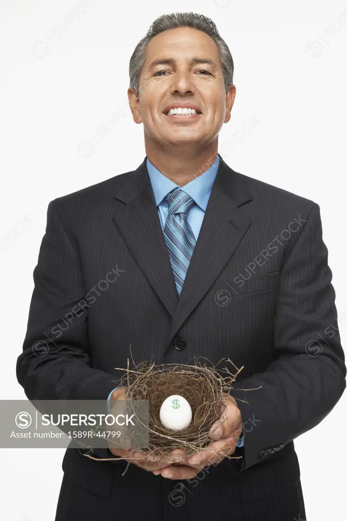 Hispanic businessman holding nest with dollar sign egg