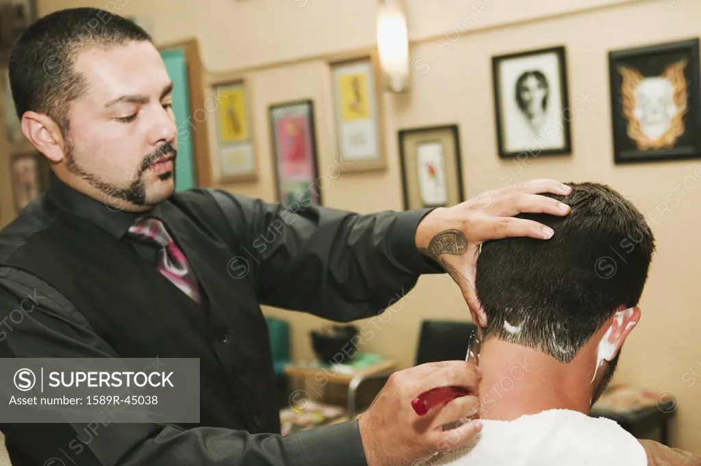Hispanic barber shaving mans neck