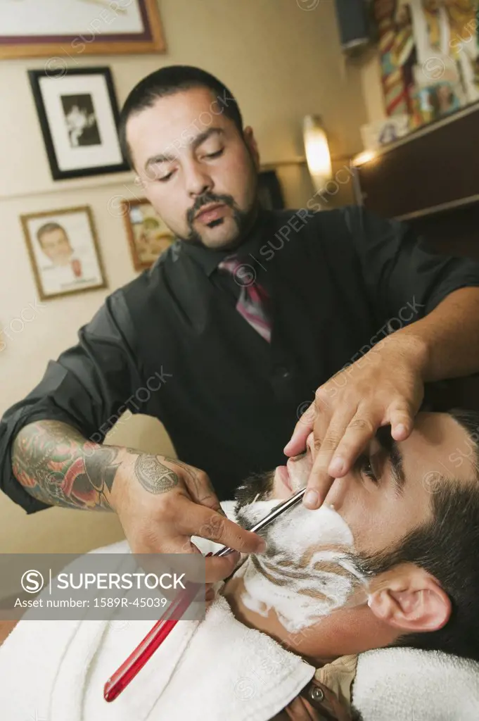 Hispanic barber shaving mans face