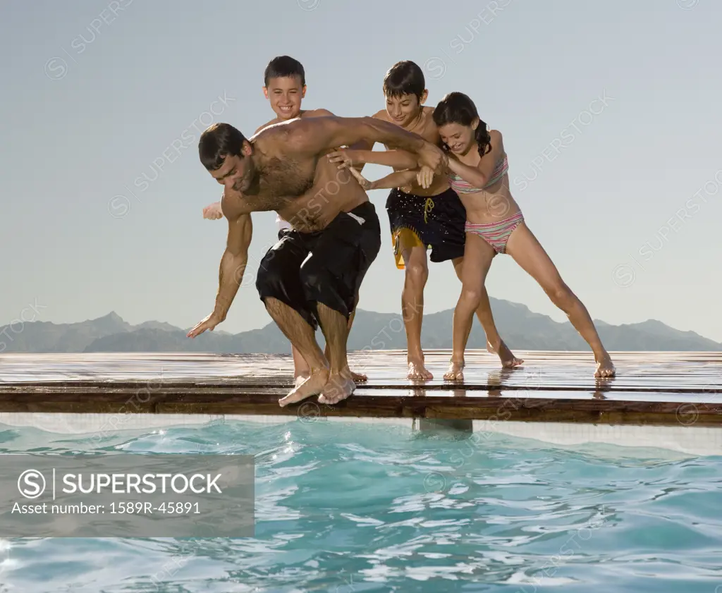 Hispanic children pushing father into swimming pool