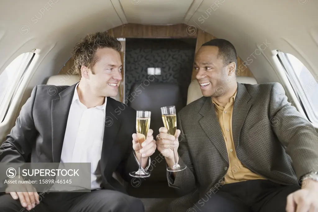 Multi-ethnic businessmen toasting on airplane