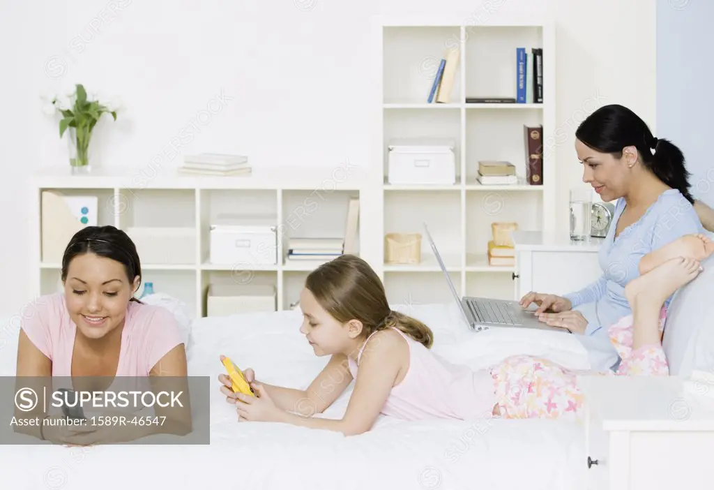 Hispanic mother and daughters relaxing on bed