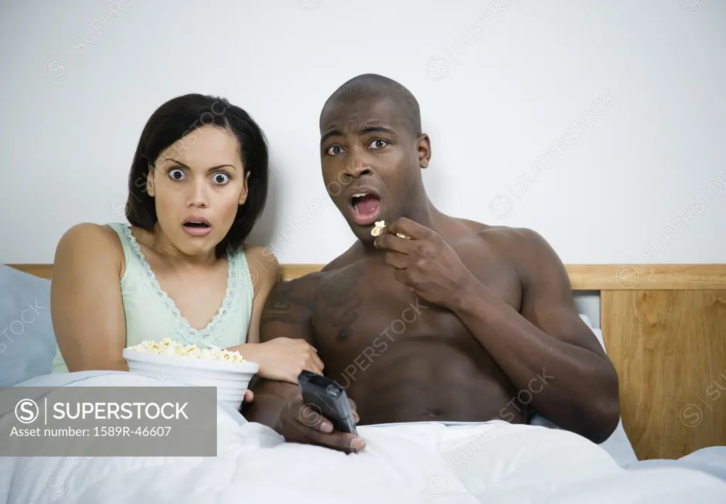 Multi-ethnic couple watching movie in bed
