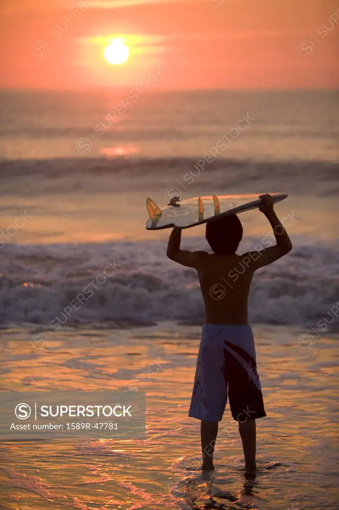 Asian boy holding surfboard at beach