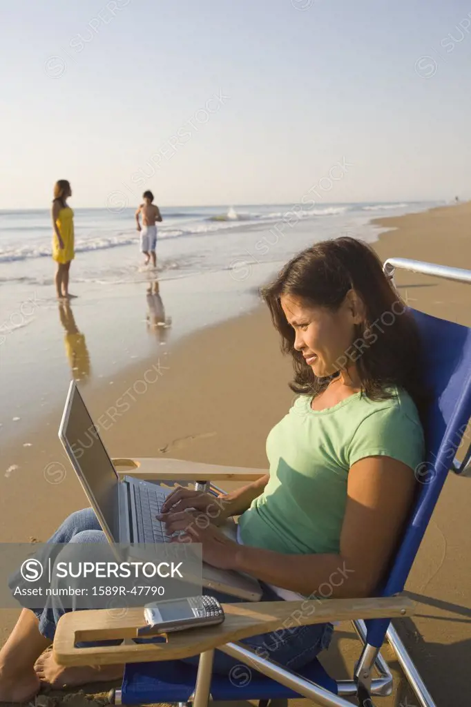 Asian woman typing on laptop at beach