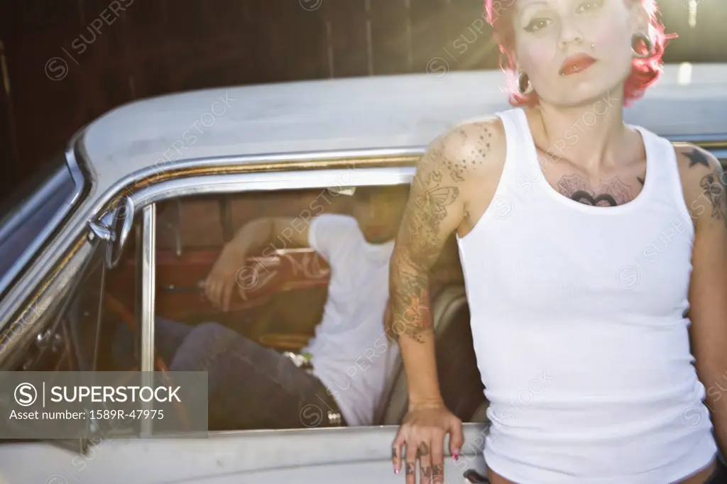Tattooed Hispanic woman leaning on car