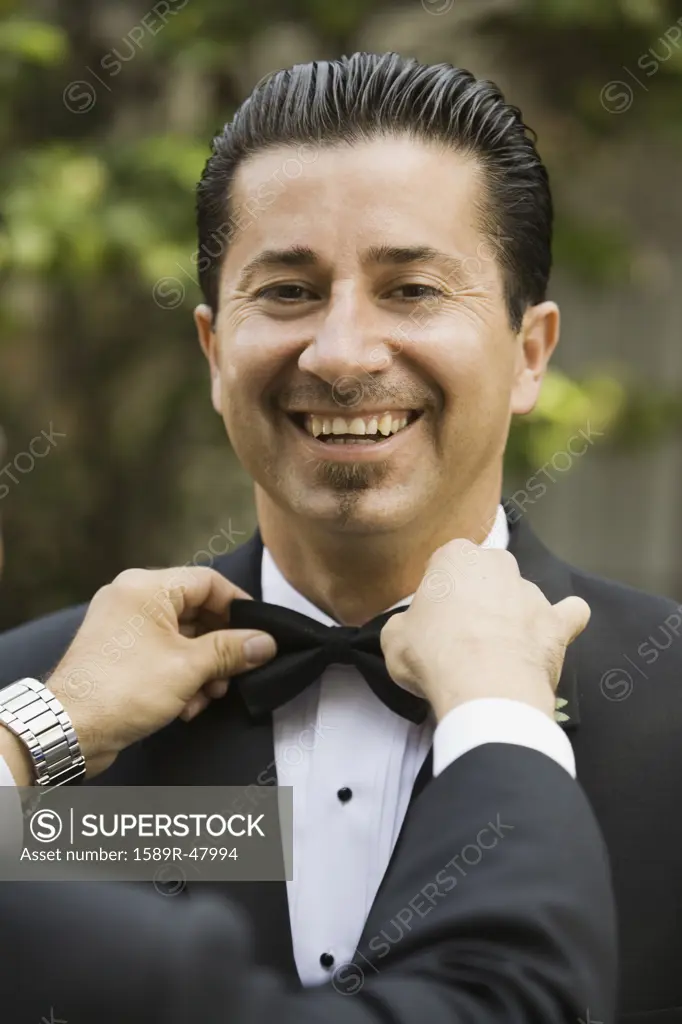 Hispanic man having bowtie adjusted