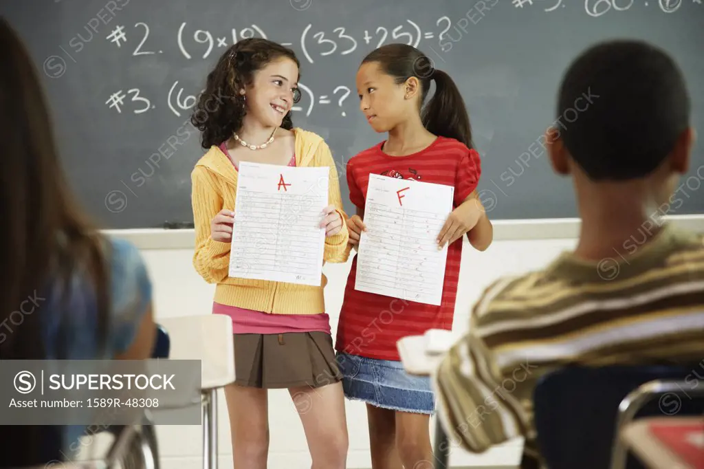 Multi-ethnic girls holding papers in front of class