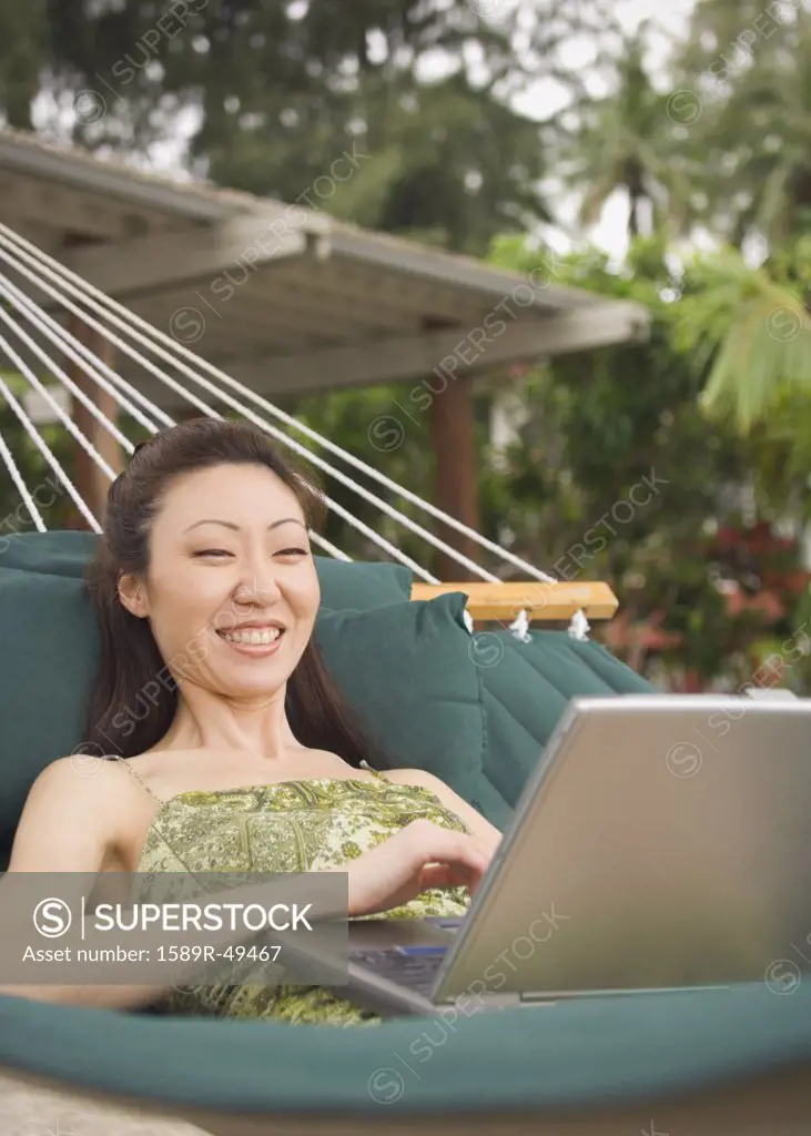 Asian woman with laptop in hammock