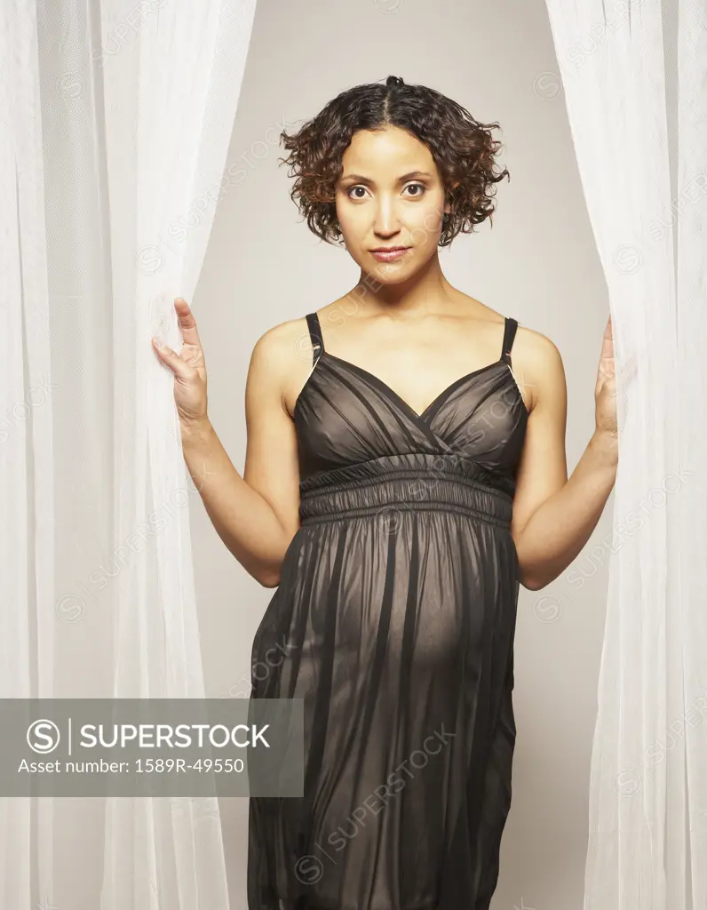 Pregnant Mixed Race woman standing in curtains